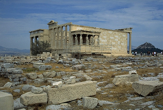 General view of the Erechtheion from the southwest, showing the North Porch (at left), the Olive Tree of Athena (modern replacement!), and the Carytatid Porch. - Note the modern (white) blocks of Pentelic marble which have been used in the reconstruction of the building. The blue limestone foundations of the Old Athena Temple (built c. 510-500 BC and destroyed by the Persians in 480 BC) are visible south of the E by Kevin T. Glowacki and Nancy L. Klein