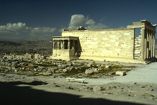 View of the south and east sides of the Erechtheion. The blue limestone foundations of the Old Athena Temple (built c. 510-500 BC and destroyed by the Persians in 480 BC) are visible in the foreground. - Photo taken in 1989, from the southeast (from the northern pteron of the Parthenon). by Kevin T. Glowacki and Nancy L. Klein