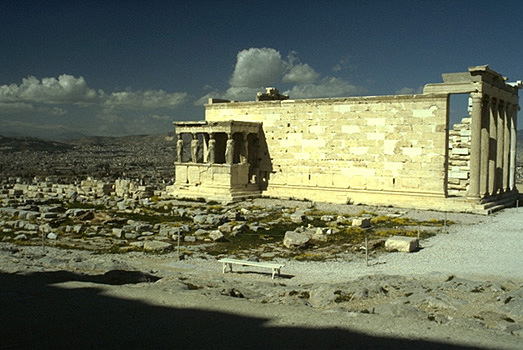 View of the south and east sides of the Erechtheion. The blue limestone foundations of the Old Athena Temple (built c. 510-500 BC and destroyed by the Persians in 480 BC) are visible in the foreground. - Photo taken in 1989, from the southeast (from the northern pteron of the Parthenon).